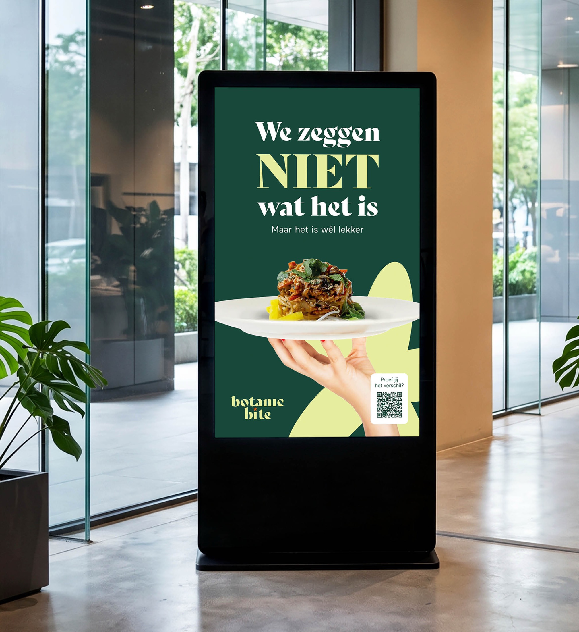 Digitale campagnemockup van BotanicBite in een kantoorfoyer — poster We zeggen NIET wat het is, maar het is wél lekker